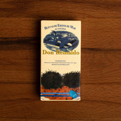 A rectangular box depicting a drawing of the cannery and two sea urchins in their spiny shells on a bed of orange sea urchin roe.