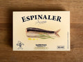 Rectangular, cream-coloured card box with an image of a sardine by a frond of dill and some drops of olive oil. Espinaler is written in black lettering above the image.