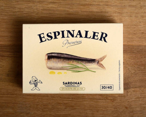 Rectangular, cream-coloured card box with an image of a sardine by a frond of dill and some drops of olive oil. Espinaler is written in black lettering above the image.
