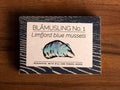 A tin with a drawing of a blue mussel on the front and dark blue waves round the border