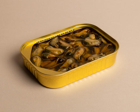 An open golden tin of mussels in a clear oil, against a pale backdrop.