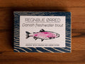 A tin with a blue border and a drawing of a trout coloured pink on the front