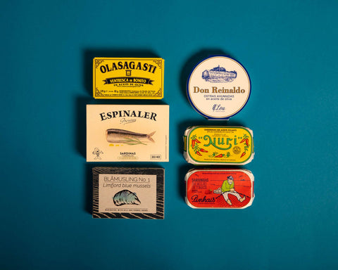 Six brightly coloured tins arranged on a light blue backdrop.