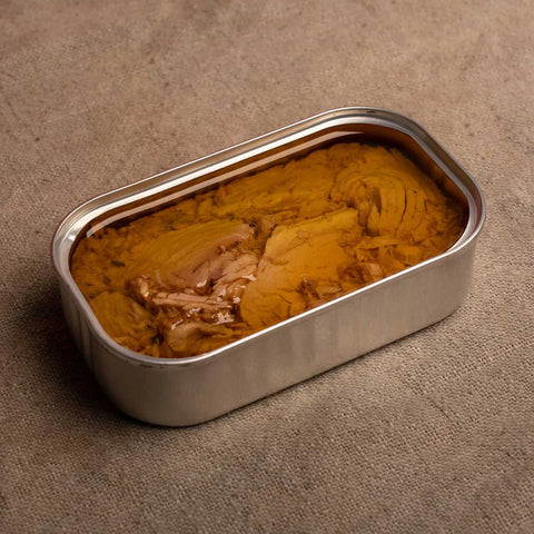 An open silver-coloured tin of tuna in olive oil on a grey-brown pleated background.
