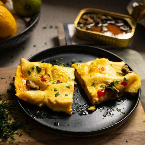 Smoked mussel omelette seasoned with thyme and garlic. Presented on a black plate on a light wooden chopping board.