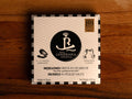 Tinned mussels in black and white card packaging with a small illustration of an open mussel on the front. The tin is against a wood background.