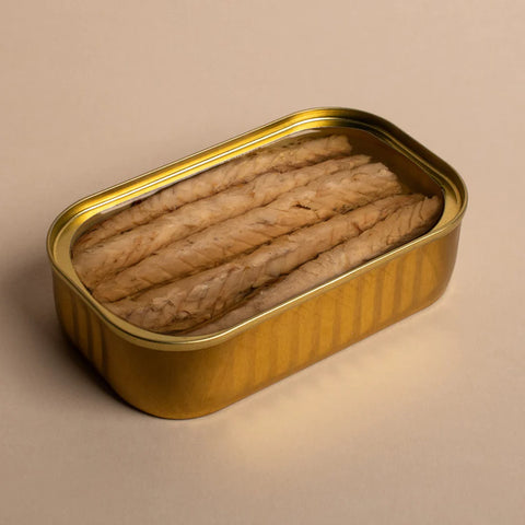 An open, gold-coloured tin with mackerel fillets in olive oil inside. The tin is on a pale background.