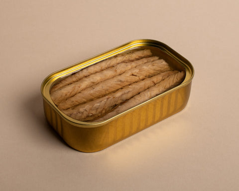 An open, gold-coloured tin with mackerel fillets in olive oil inside. The tin is on a pale background. 
