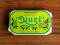 A tin of mackerel fillets in a green paper wrap with Nuri written in green lettering above some small olive branches.