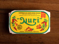 A tin of sardines in yellow packaging with Nuri written in green lettering and images of red chilli peppers and flames on the front