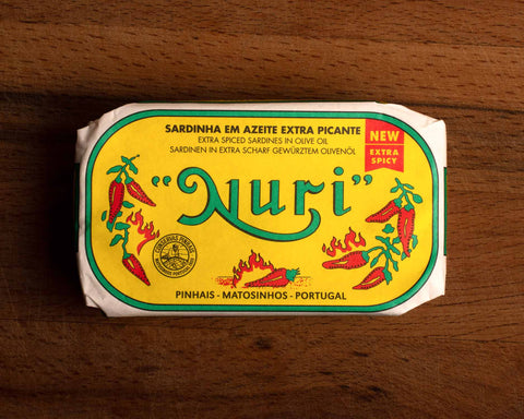 A tin of sardines in yellow packaging with Nuri written in green lettering and images of red chilli peppers and flames on the front