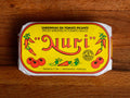 A tin of sardines in spicy tomato in a yellow paper wrap with a white and red border. Nuri is written in red above images of tomatoes and red chilli peppers.