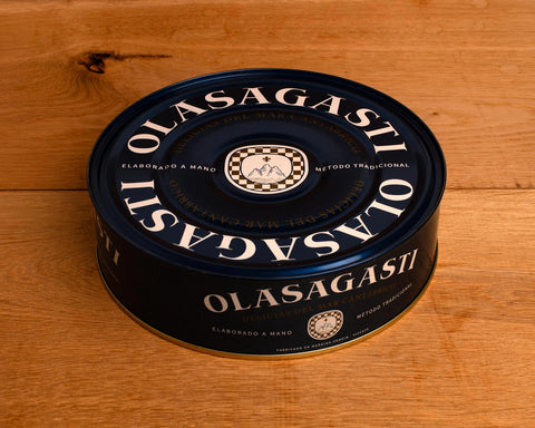 A large circular tin of tuna with a red lid with gold lettering and an image of a golden tuna on the front against a blue and red background.