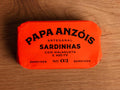 A tin of sardines with chilli and olive oil in bright red packaging, featuring the Papa Anzois brand name at the top.