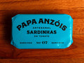 A tin of sardines in tomato sauce in blue packaging, with Papa Anzóis displayed at the top.