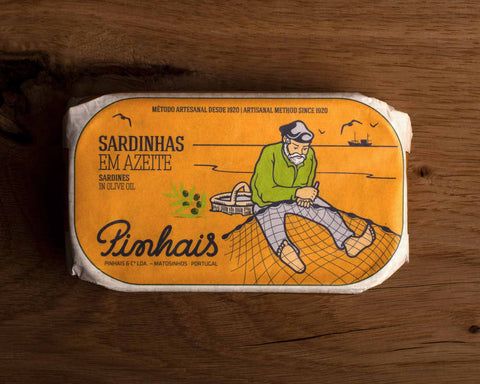 Tinned sardines in an orange paper wrap with an image of a fisherman mending a fishing net by the Pinhais logo.
