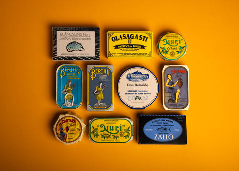 A selection of brightly-packaged tinned fish on a yellow backdrop