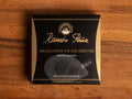 A tin of mussels in black card packagaing with a gold border and an image of a mussel drawn on grey on the front. The tin is on a wood background.