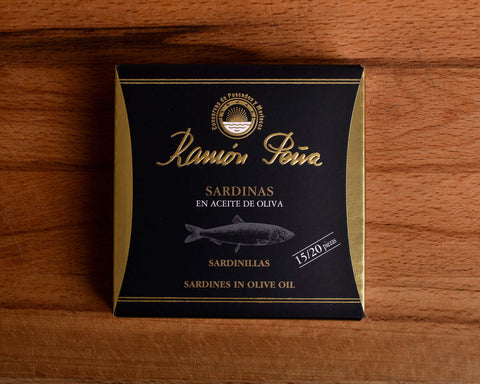 Sardines in olive oil in black and gold card packaging. Ramón Peña is written in raised gold lettering above a silver-grey image of a sardine.