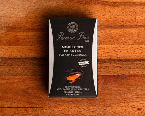 A tin of spicy mussels in a rectangular silver and black box with nautical cartoons on the silver border.