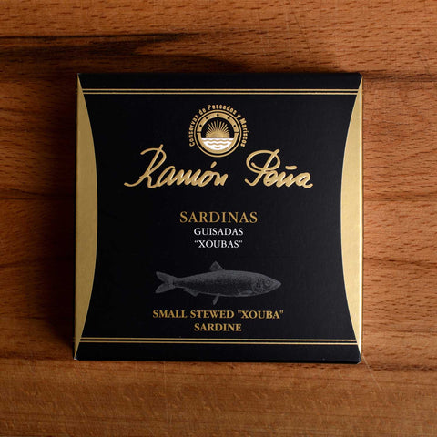 A tin of Ramon Pena stewed xouba sardines in black card packaging, featuring an illustration of a sardine.