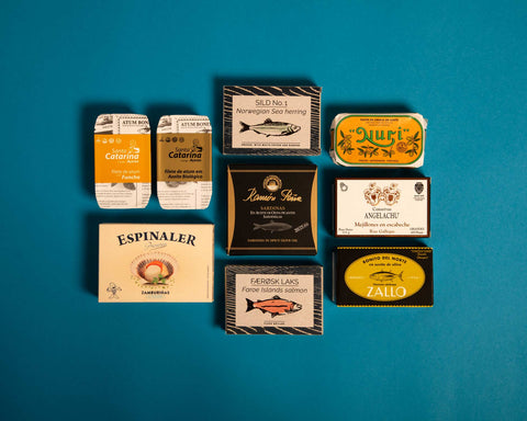 A selection of tinned fish in classic and colourful packaging on a light blue backdrop