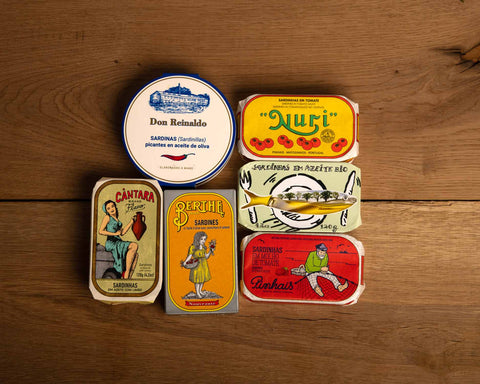A selection of colourfully-packaged tinned sardines against a wooden background.
