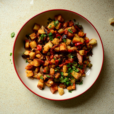 Sardine migas neatly placed on a plate with strong vibrant colours. Garnished with chopped parsley.