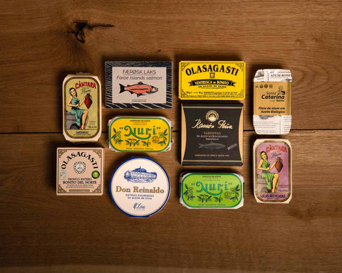 A selection of colourfully-packaged tinned fish against a wood background.