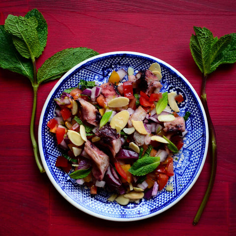 Squid in olive oil added to salad with chopped mint. Garnished with almonds, placed in a blue plate on a wine wooden background.