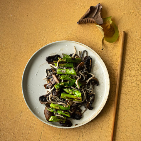 Surimi eels with asparagus and mushrooms on a cream plate against a gold background.
