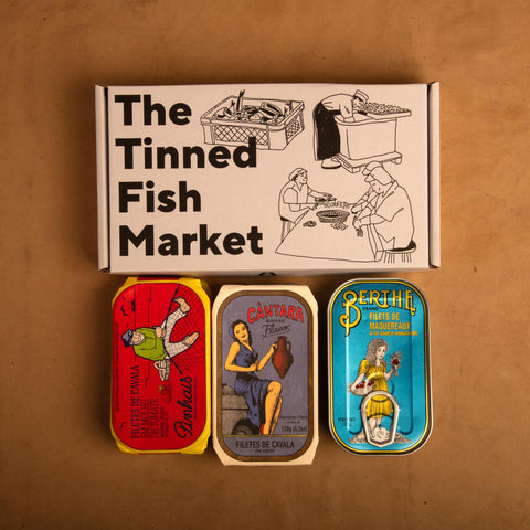 Three colourfully packaged tins of fish beneath a gift box illustrated with line drawings of the cannery workers, a basket of fish and The Tinned Fish Market in bold black lettering.