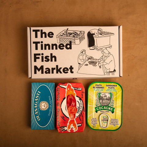 Three colourfully packaged tins of fish beneath an illustrated gift box