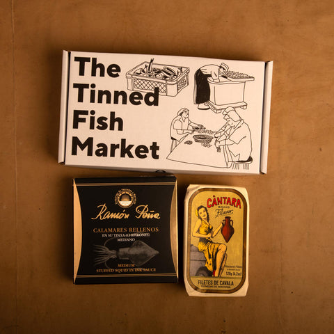 Two tins of fish beneath an illustrated gift box