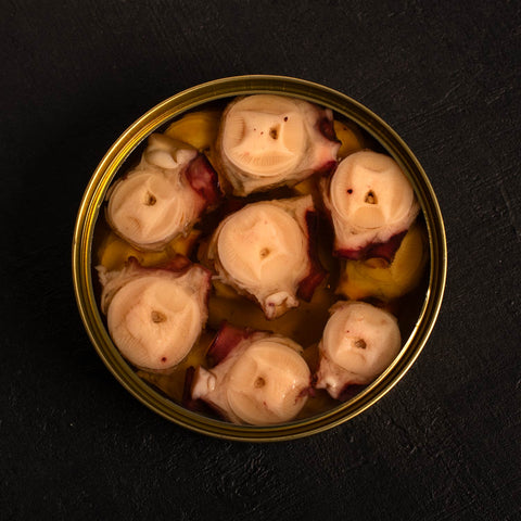 open tin of octopus in a clear olive oil. the octopus is cut in slices. the background is a black wood board