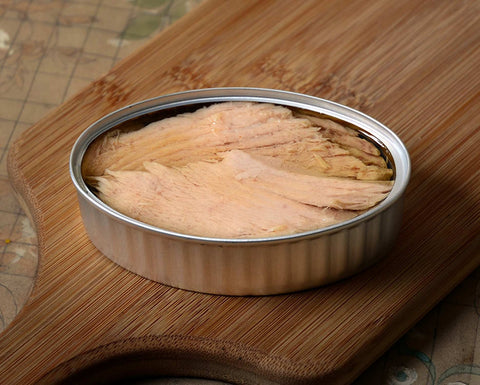 An open tin of thinly sliced ventresca tuna belly in olive oil on a narrow chopping board.