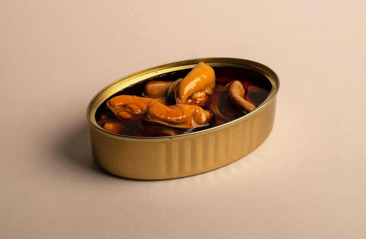 open tin of plump mussels. the mussels are burn orange, the tin is  brass, the backdrop is off white