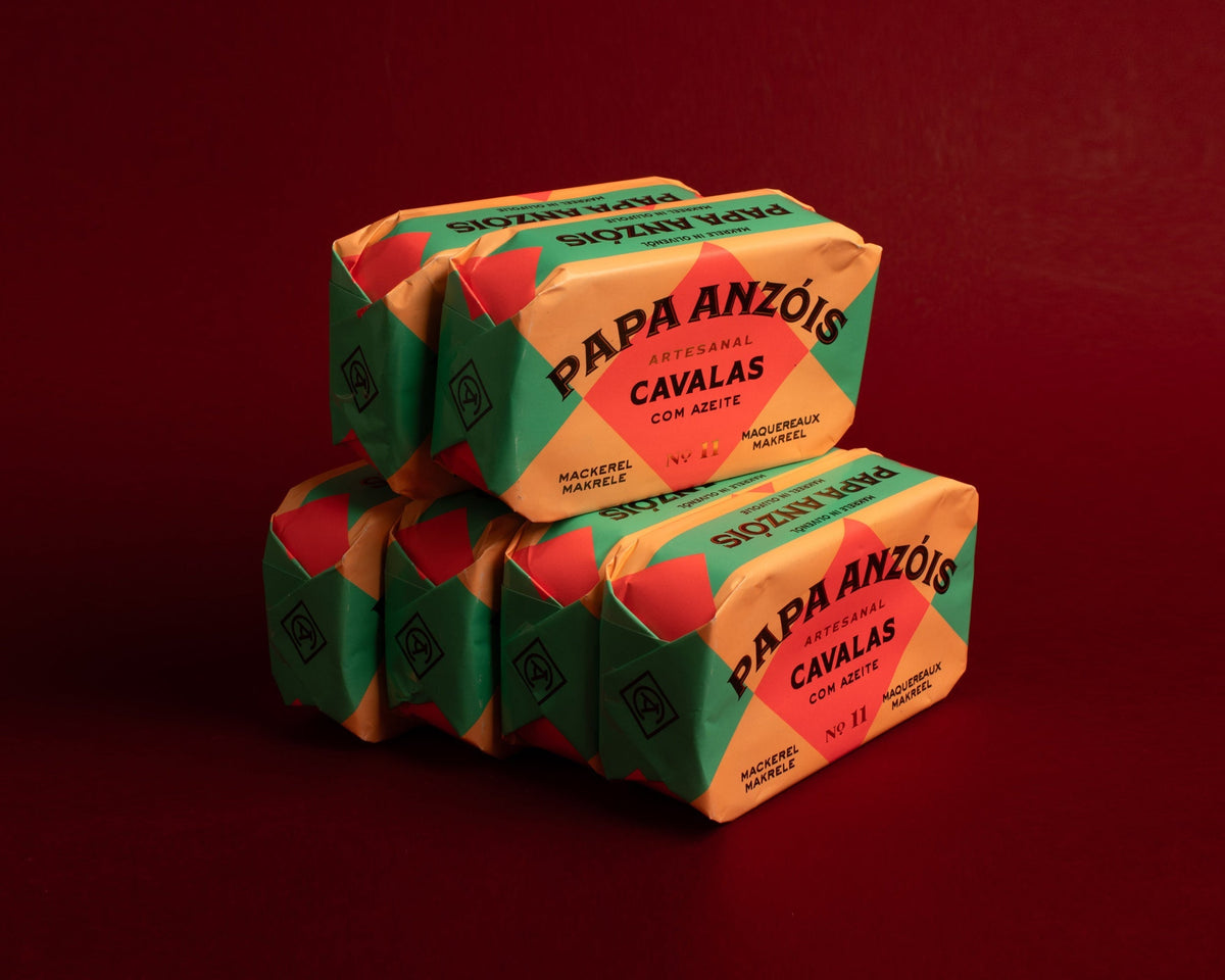 A stack of brightly packaged Papa Anzois tinned mackerel against a red background.