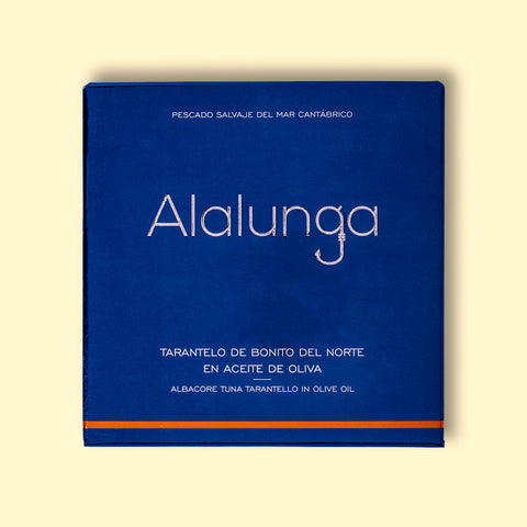 Canned white tuna in square blue card packaging with Alalunga in silver, embossed lettering above a diagram of a tuna. There is a copper stripe along the bottom of the packaging.