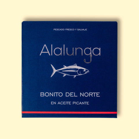 Canned white tuna in square blue card packaging with Alalunga in silver, embossed lettering above a diagram of a tuna. There is a red stripe along the bottom of the packaging.