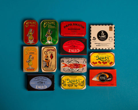 A selection of colourfully-packaged tinned sardines, tuna, mackerel and mussels against a blue background.