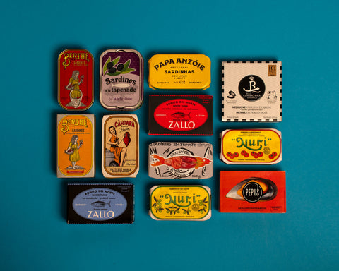 A selection of colourfully-packaged tinned sardines, tuna, mackerel and mussels against a blue background.