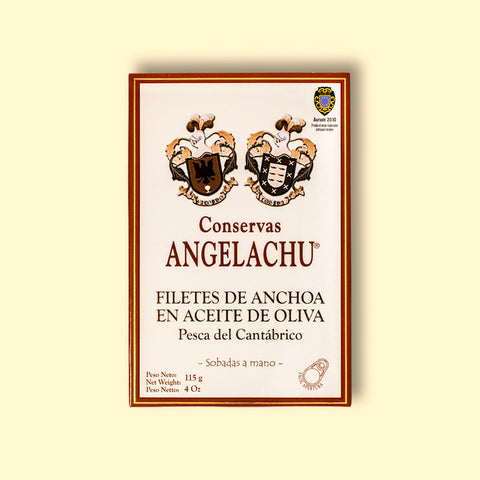A tin of large Cantabrian anchovies in rectangular cream packaging with a brown border, against a pale yellow wood background.