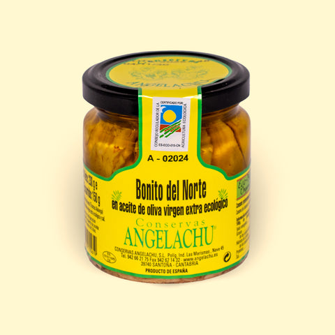 A jar of white tuna fillets in a golden-coloured extra virgin olive oil. There is a green and yellow label on the jar with Bonito del Norte written in black lettering and Conservas Angelachu written in green beneath.