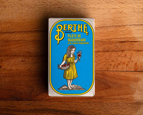 A bright blue tin with Berthe written in yellow lettering above an image of a little girl holding a bunch of flowers and wearing a yellow dress.