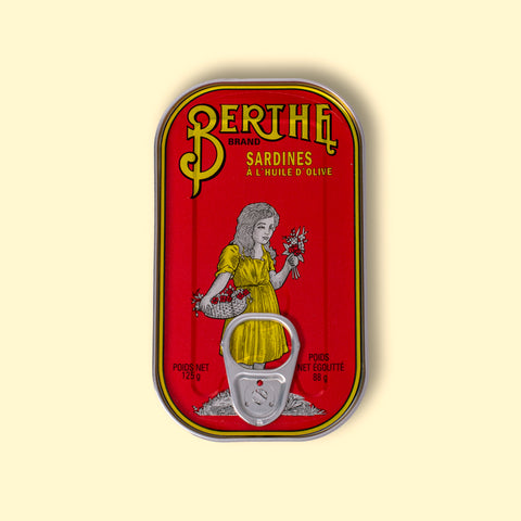 A red tin with Berthe written in yellow above an illustration of a little girl holding a bunch of flowers and wearing a yellow dress.