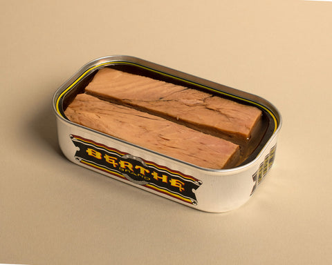 tinned tuna, opened in a silver tin with gold trimming in front of a beige backdrop