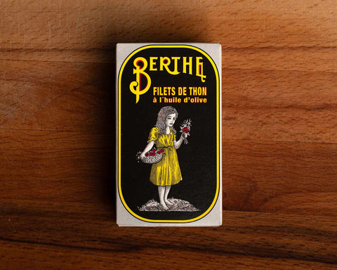 A tin of tuna with Berthe written in yellow on a black background above a girl in a yellow dress carrying a basket of flowers.