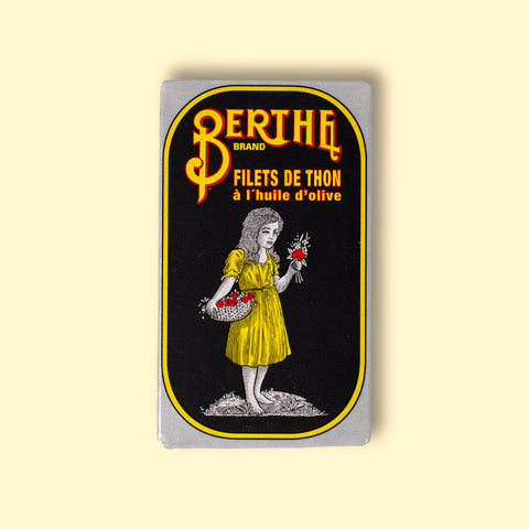 A tin of tuna with Berthe written in yellow on a black background above a girl in a yellow dress carrying a basket of flowers.