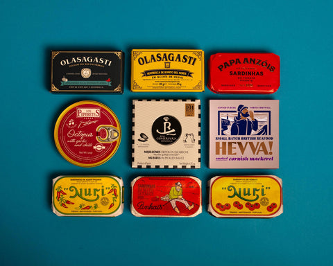 A selection of colourfully-packaged tinned sardines, tuna belly, octopus and mussels  against a blue background.